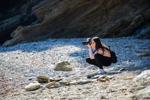 Beautiful woman crouching taking a picture of a pebbles beach at a creek side shot