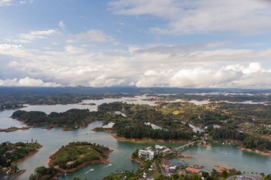 Antioquia, Kolombiya 'daki Guatape rezervuarını gösteren panoramik bir manzara, birbirine bağlı adaları, su kanallarını ve yakındaki kentsel ve kırsal manzaraları vurguluyor..