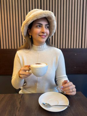 Kafede beyaz yün şapkalı beyaz elbiseler giyen güzel bir ortadoğulu genç bayan. Yüksek kalite fotoğraf