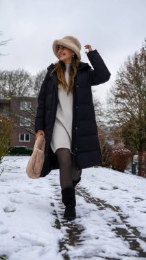 Karda, siyah ceketli, beyaz yün şapkalı ve eldivenli güzel bir orta doğulu genç kadın. Yüksek kalite fotoğraf