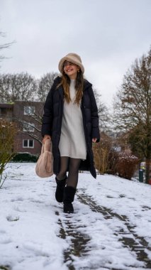 Karda, siyah ceketli, beyaz yün şapkalı ve eldivenli güzel bir orta doğulu genç kadın. Yüksek kalite fotoğraf