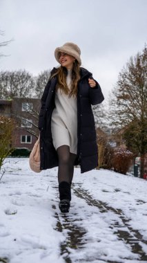 Karda, siyah ceketli, beyaz yün şapkalı ve eldivenli güzel bir orta doğulu genç kadın. Yüksek kalite fotoğraf