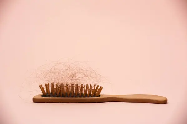 Pembe arka planda saçı dökülmüş ahşap saç fırçası.