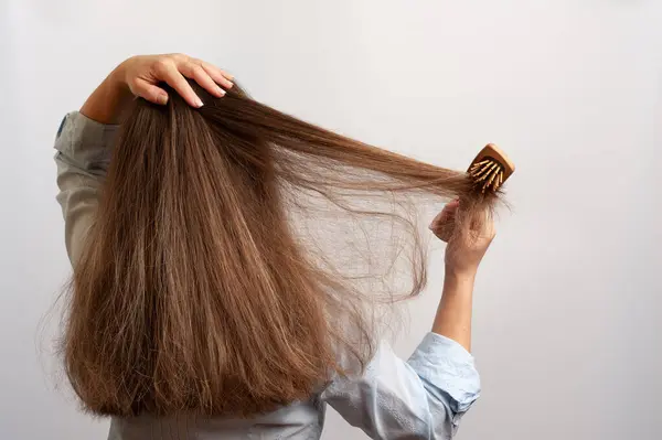 Bir kadın saçını ahşap bir saç fırçasıyla tarar.