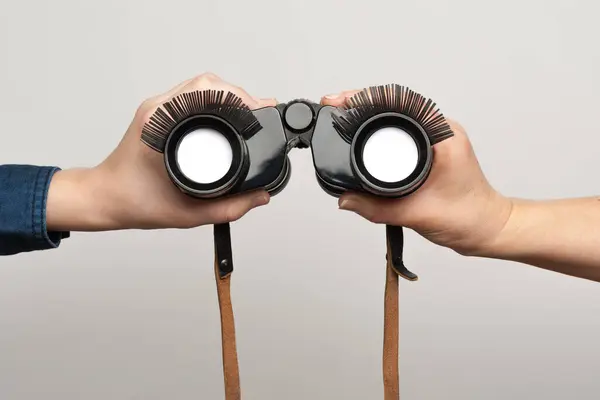 İnsan elleri komik, sahte kirpiklerle dürbün tutuyor.