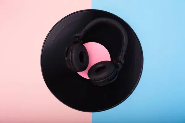 Pembe ve mavi arka planda siyah kablosuz kulaklık ve vinil kayıt.