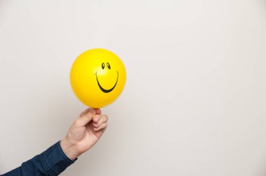 İnsan eli beyaz arka planda sarı bir gülümseme balonu tutuyor.