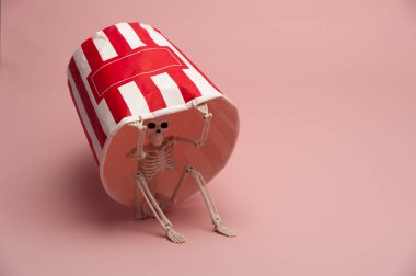 Pembe arka plandaki kağıt bardağın altındaki gizli oyuncak iskeleti.