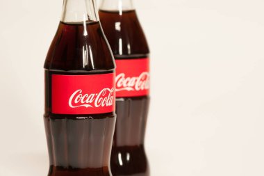 Açık gri zemin üzerinde Coca-Cola ve logosu olan cam şişeler.