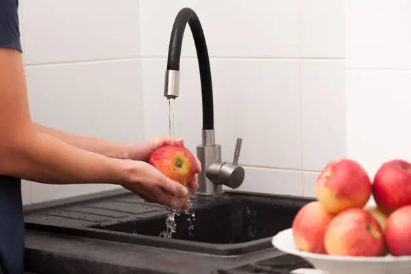 Kadın elleri mutfakta kırmızı elmaları yıkıyor.