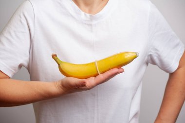 a woman shows the process of putting a condom on a penis using a banana fruit as an example