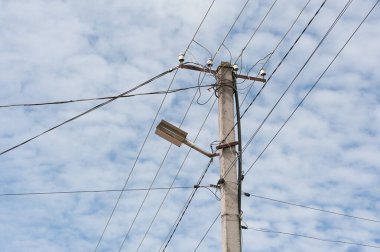 Gökyüzü arka planında kaotik kablo bağlantısı olan beton elektrik direği.