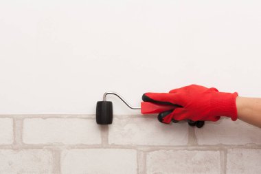 Kırmızı eldivenli bir işçinin eli bir silindir tutuyor. Duvar kağıdı yapıştırma işlemi