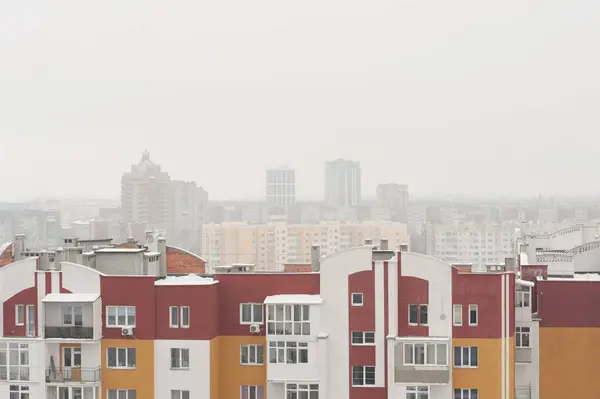 Sisli şehrin eski bölümündeki evlerin karla kaplı çatılarında yeni bir binanın penceresinden manzara