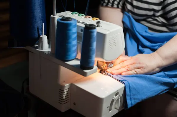 Evde elbise dikmek için dikiş makinesini kullanan bir kadının elleri.