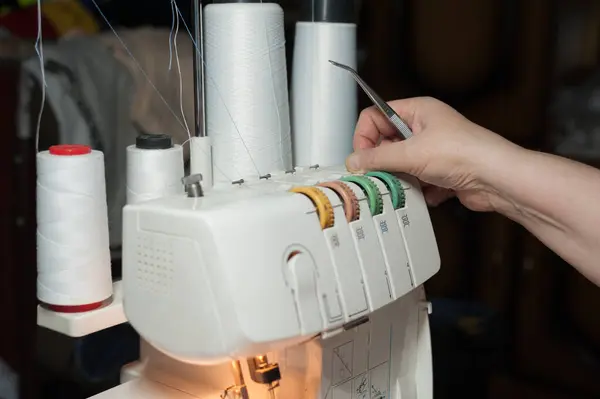 Evde elbise dikmek için dikiş makinesini kullanan bir kadının elleri.