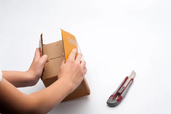 Beyaz arka plandaki paketi açarken insan eli bir bıçak tutuyor.