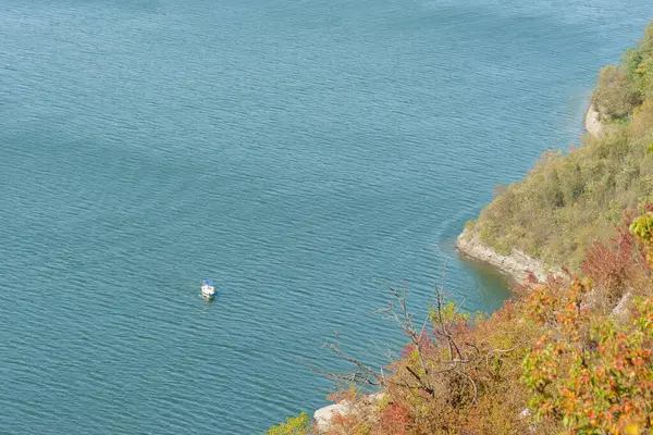 Kayalık kıyıya yakın beyaz bir tekne masmavi suyun dalgalı yüzeyinde yüzer.