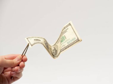 hand holding tweezers with one hundred dollar bill on the white background clipart