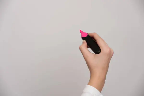 Açık gri arka planda pembe keçeli kalem tutan bir koç.