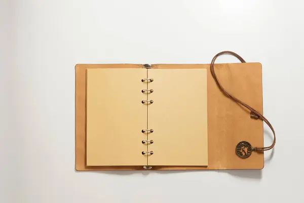 Açık bir defter, sarı boş sayfalar, güzel bir deri ambalaj ve açık gri bir arkaplan üzerine dekoratif bağlama tılsımı..
