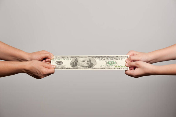 две пары человеческих рук протягивающих стодолларовую купюру