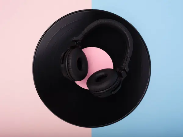 Pembe ve mavi arka planda siyah kablosuz kulaklık ve vinil kayıt.