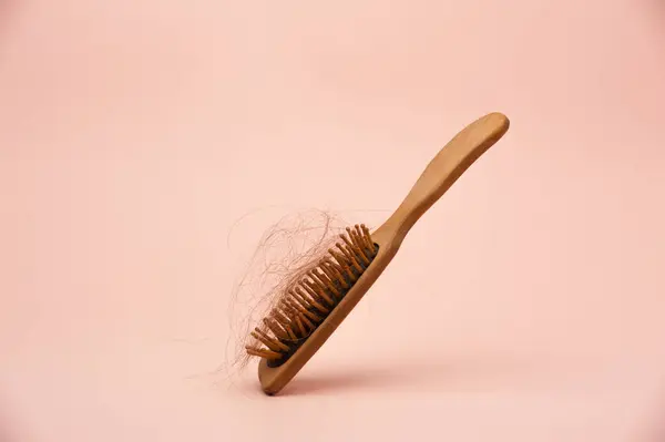 Pembe arka planda saçı dökülmüş ahşap saç fırçası.