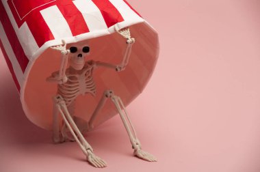 Pembe arka plandaki kağıt bardağın altındaki gizli oyuncak iskeleti.