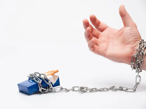 Hapis ve tütün bağımlılığını sembolize eden bir zincirle bir paket sigaraya bağlanmış bir insan eli.