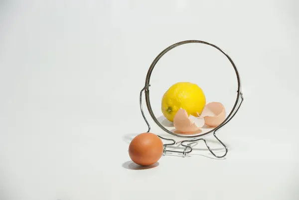 Yumurta kabuğu ve limon beyaz arka plandaki aynada yansıtılır..