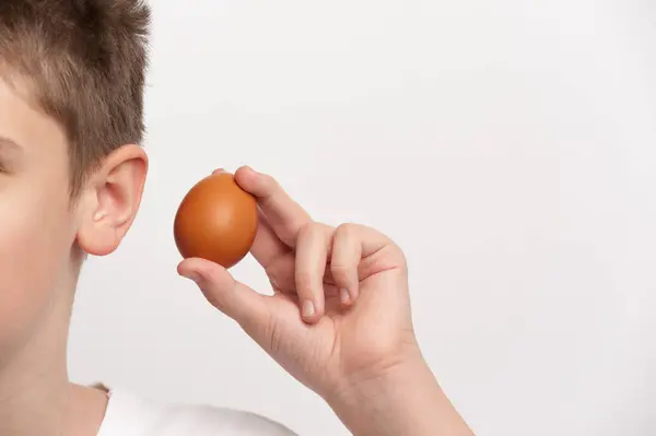 Bir genç, yumurtayı kulağına tutarak dinler.