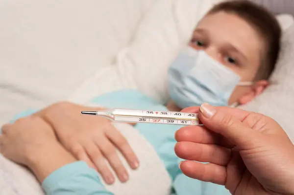 Hasta bir çocuğun arka planında bir hemşirenin elinde termometre.