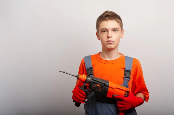 İş üniformalı genç bir çocuğun elinde elektrikli matkap var.