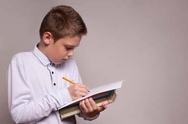 Elinde kitap yığını olan okul çocuğu elinde bazı notlar tutuyor.