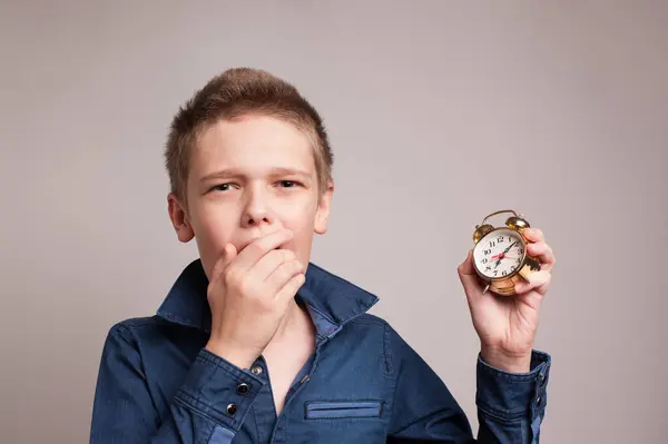 Uykulu çocuk elinde çalar saatle esniyor.