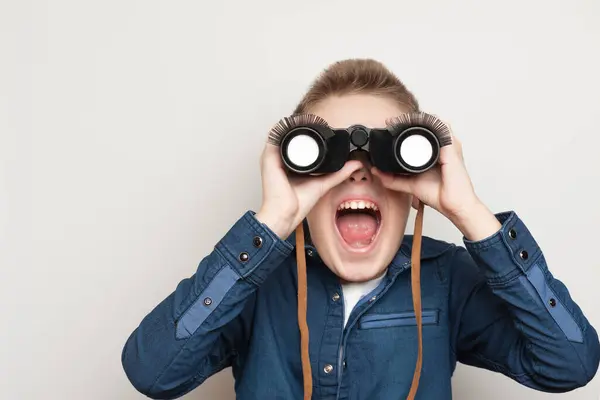 Komik takma kirpiklerle dürbünle bakan neşeli çocuk.