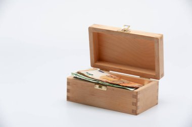 Beyaz arka planda içi para dolu küçük tahta bir kutu..