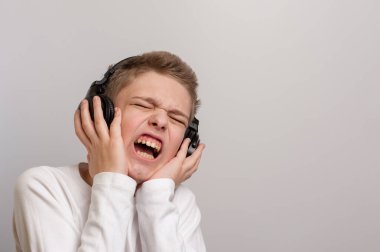 Yüz ifadesi bozuk bir çocuk kulaklıklardan yüksek sesle müzik dinliyor.