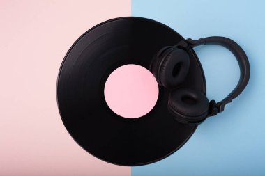 Pembe ve mavi arka planda siyah kablosuz kulaklık ve vinil kayıt.