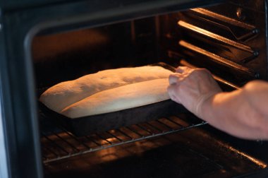 Ev yapımı ekmek pişirmenin başlangıcı. Fırıncı bir hamur ile kalıpları fırına sokuyor.