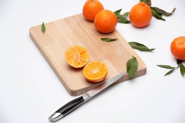 Meyve kompozisyonu. Ağaç kesme tahtasının üzerinde yapraklar ve kesilmiş meyvelerle sulu mandalinalar var.