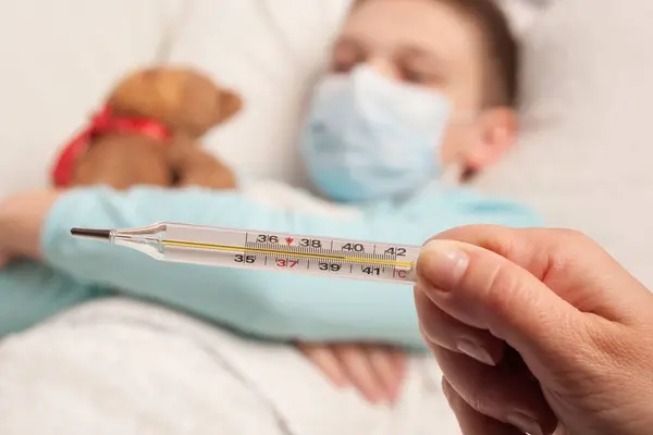 Hasta bir çocuğun arka planında bir hemşirenin elinde termometre.
