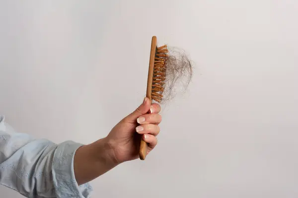 Kadının elleri saç fırçasını tutarken bir tutam yırtık saçı gösteriyor. Erken saç dökülmesi probleminin altını çiziyorum.