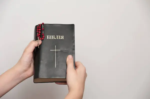 Beyaz arka planda İncil 'i tutan genç bir adamın elleri. Kitabın başlığının çevirisi: 