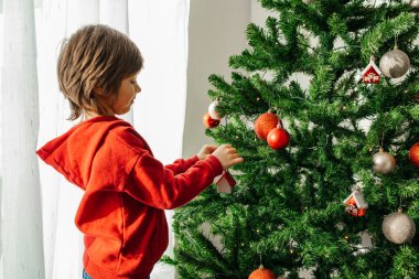 Çekici küçük bir çocuk Noel ağacına yeni yıl oyuncakları asıyor. Çocuklar yeni yılı ve Noel 'i kutluyor ve evi dekore ediyorlar.