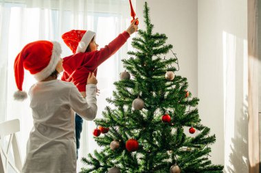 Çocuklar yeni yıl ve Noel 'i bekliyor. Kız kardeşi küçük kardeşine Noel Ağacı 'nı süslemesinde yardım ediyor..