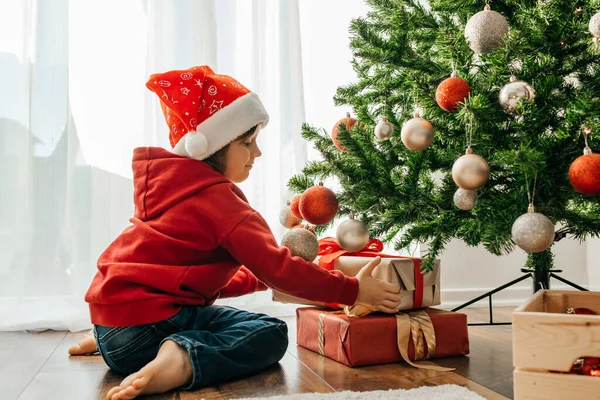 Charmig Pojke Tomte Hatt Tar Julklappar Från Nyårsträdet Och Skrattar — Stockfoto