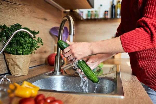 Close-up of a girls hands washing vegetables in the kitchen under the faucet. Preparing vegetables for cooking.