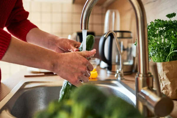 Close-up of a girls hands washing vegetables in the kitchen under the faucet. Preparing vegetables for cooking.